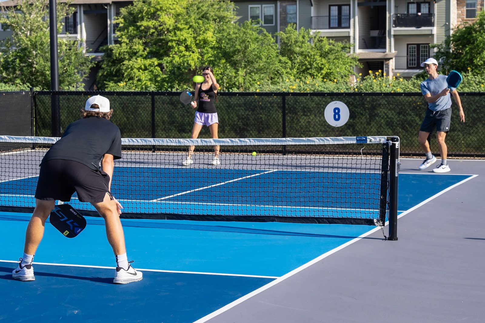 Four players mid-rally on an outdoor pickleball court at RacFit