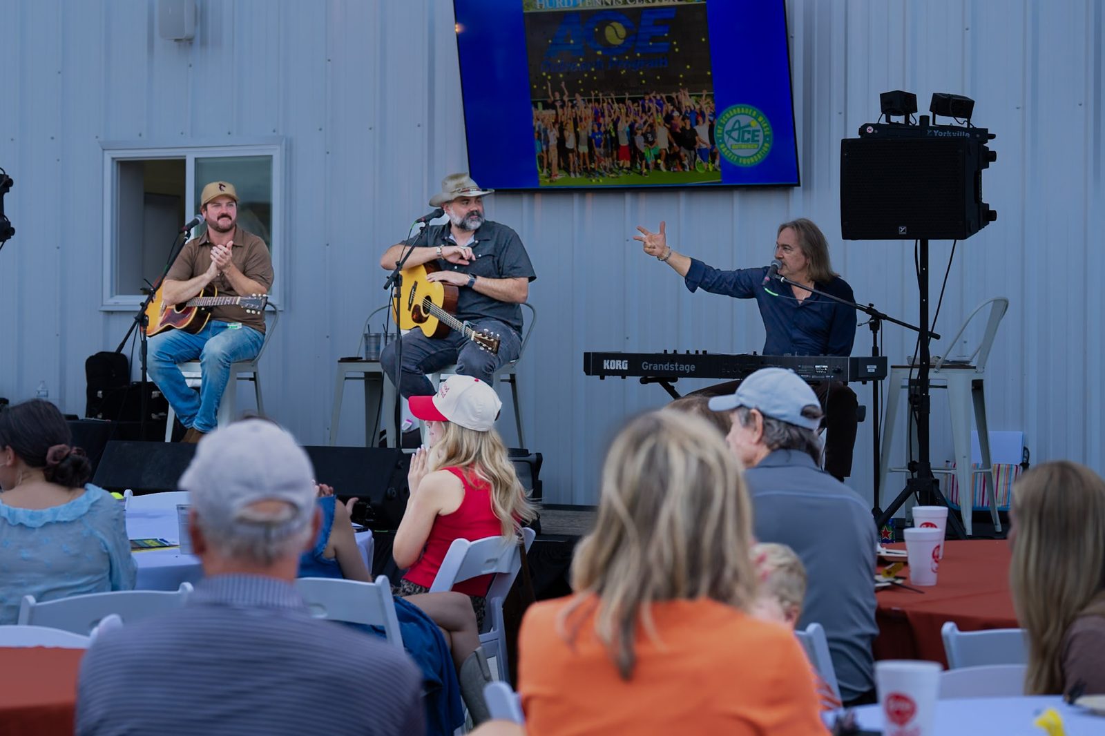 A three-piece band playing an acoustic set to a seated crowd at RacFit