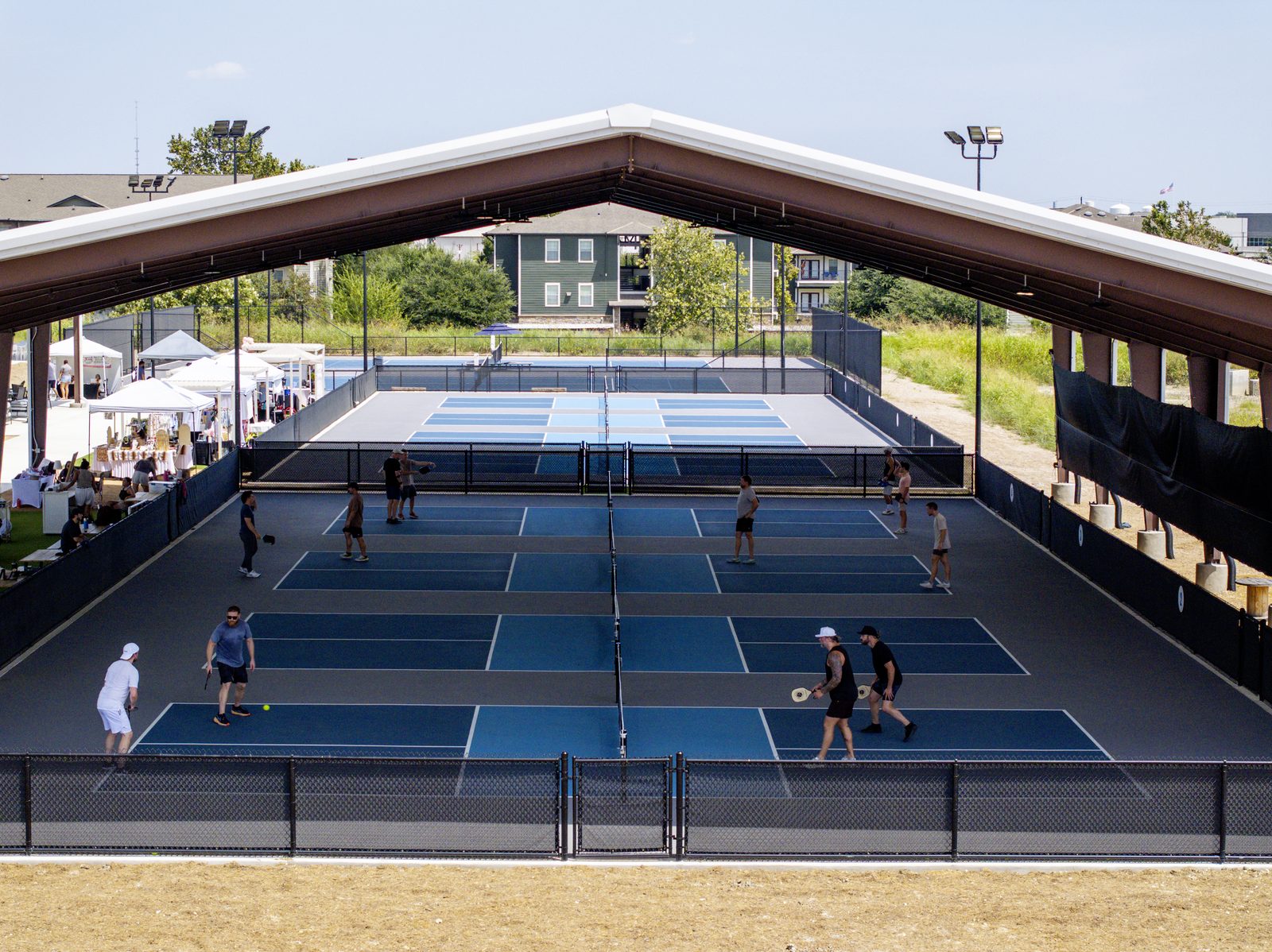 Players on the covered pickleball courts with vendor tents set up alongside