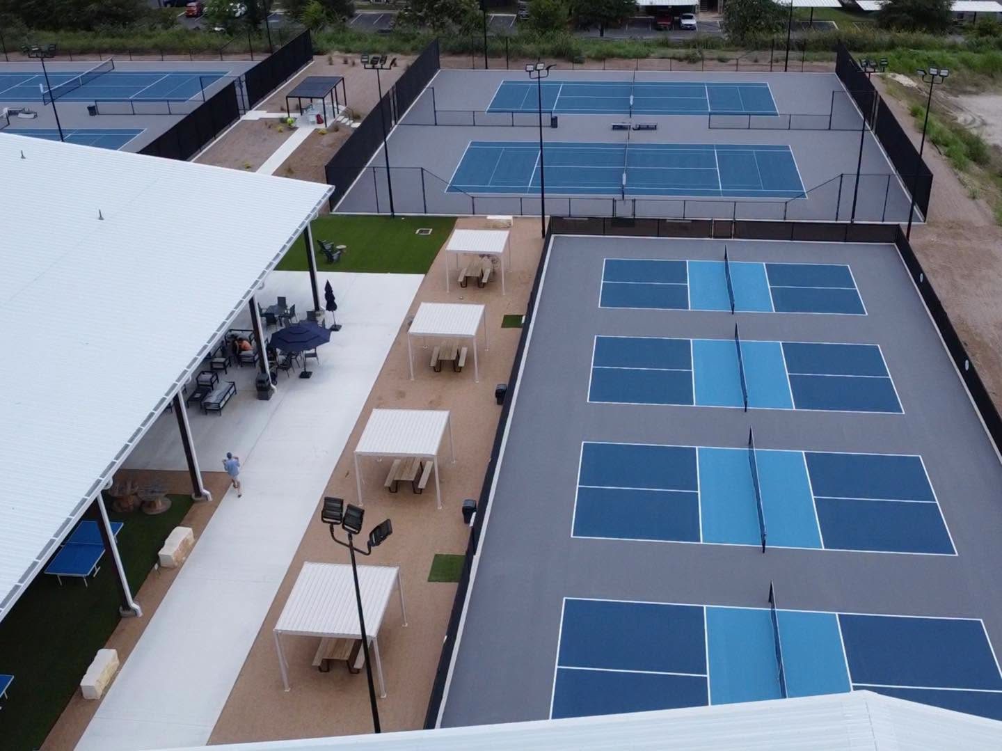 An aerial view over the RacFit tennis and pickleball courts and the shaded picnic tables between them